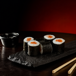 Salmon maki rolls on a dark slate plate with a small soy sauce dish and wooden chopsticks nearby.